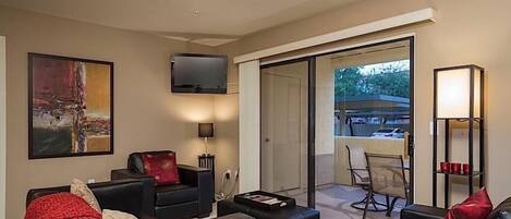 A modern living room with a flat-screen TV, a painting, and a dining area with chairs and a table.