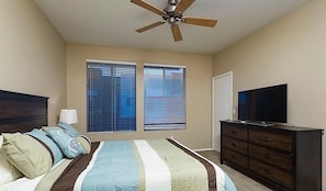 Une chambre à coucher comprenant un lit, une commode, un téléviseur et un ventilateur de plafond.