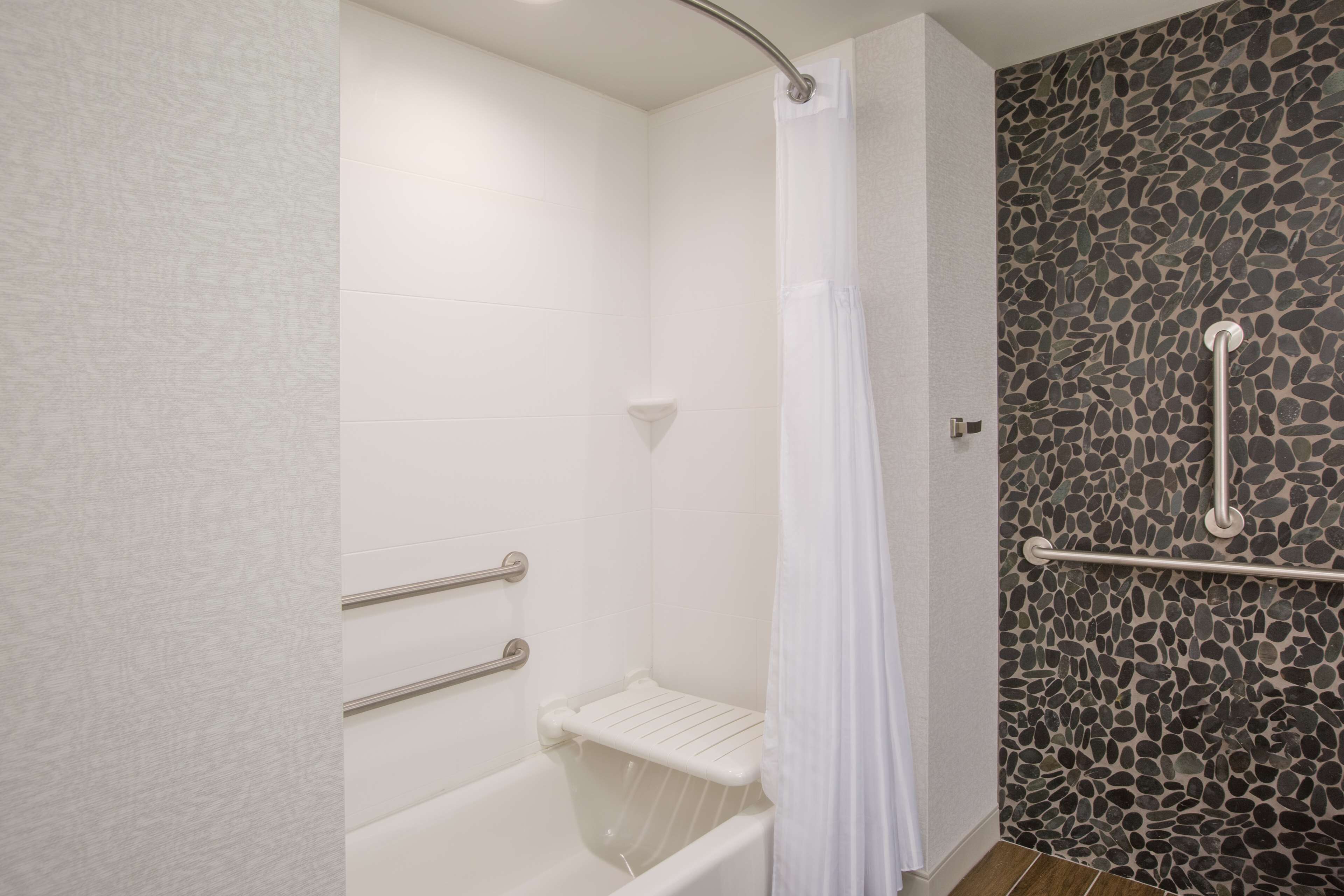 A bathroom with a bathtub, a shower with a stone wall, and a white curtain.