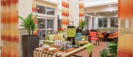 A spacious indoor area with a large table set for dining, multiple seating arrangements, and a coffee machine.