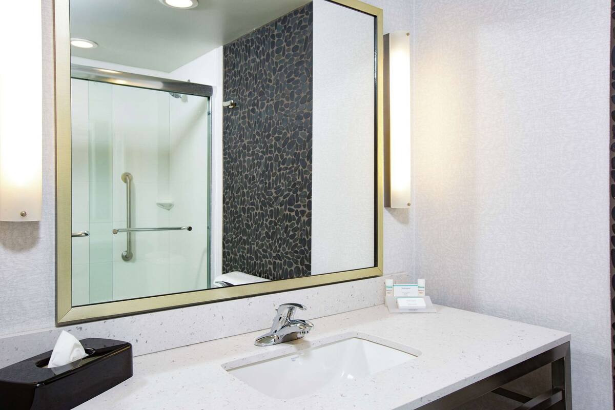A bathroom with a large mirror, a sink, and a shower.
