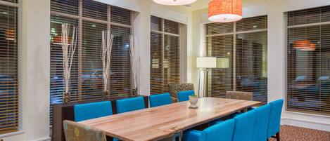 Un salón de conferencias con una larga mesa de madera, sillas tapizadas en azul y lámparas colgantes naranjas.
