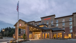 A hotel with a brick facade, a large entrance canopy, and a flagpole with an American flag. - Hilton Garden Inn Olympia (Olympia)