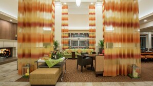 A spacious lobby with a fireplace, seating area, and a view of the lobby in the background. - Hilton Garden Inn Olympia (Olympia)