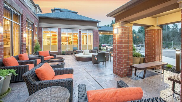 A patio area with wicker furniture, a round seating area, and a view of a building with large windows. - Hilton Garden Inn Olympia (Olympia)