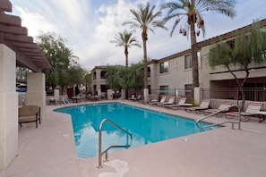 A swimming pool with lounge chairs and palm trees, surrounded by a building with multiple balconies.