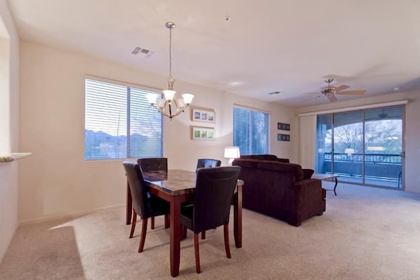 A spacious living room with a dining area, large windows, and a ceiling fan.