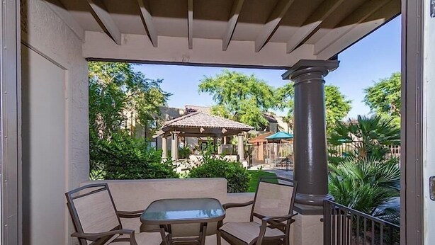 A covered patio with a table and chairs, a pergola, and a view of a park with trees and a gazebo. - Exclusively Yours By Signature Vacation Rentals (Scottsdale)