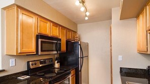 A kitchen with wooden cabinets, a stainless steel microwave, a black refrigerator, a stove, and a coffee maker. - Exclusively Yours By Signature Vacation Rentals (Scottsdale)