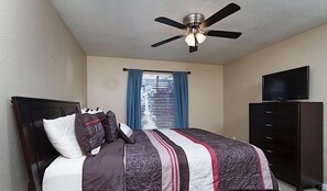 A bedroom with a bed, a ceiling fan, a window with blinds, a TV on a dresser, and a dark wooden dresser. - Exclusively Yours By Signature Vacation Rentals (Scottsdale)