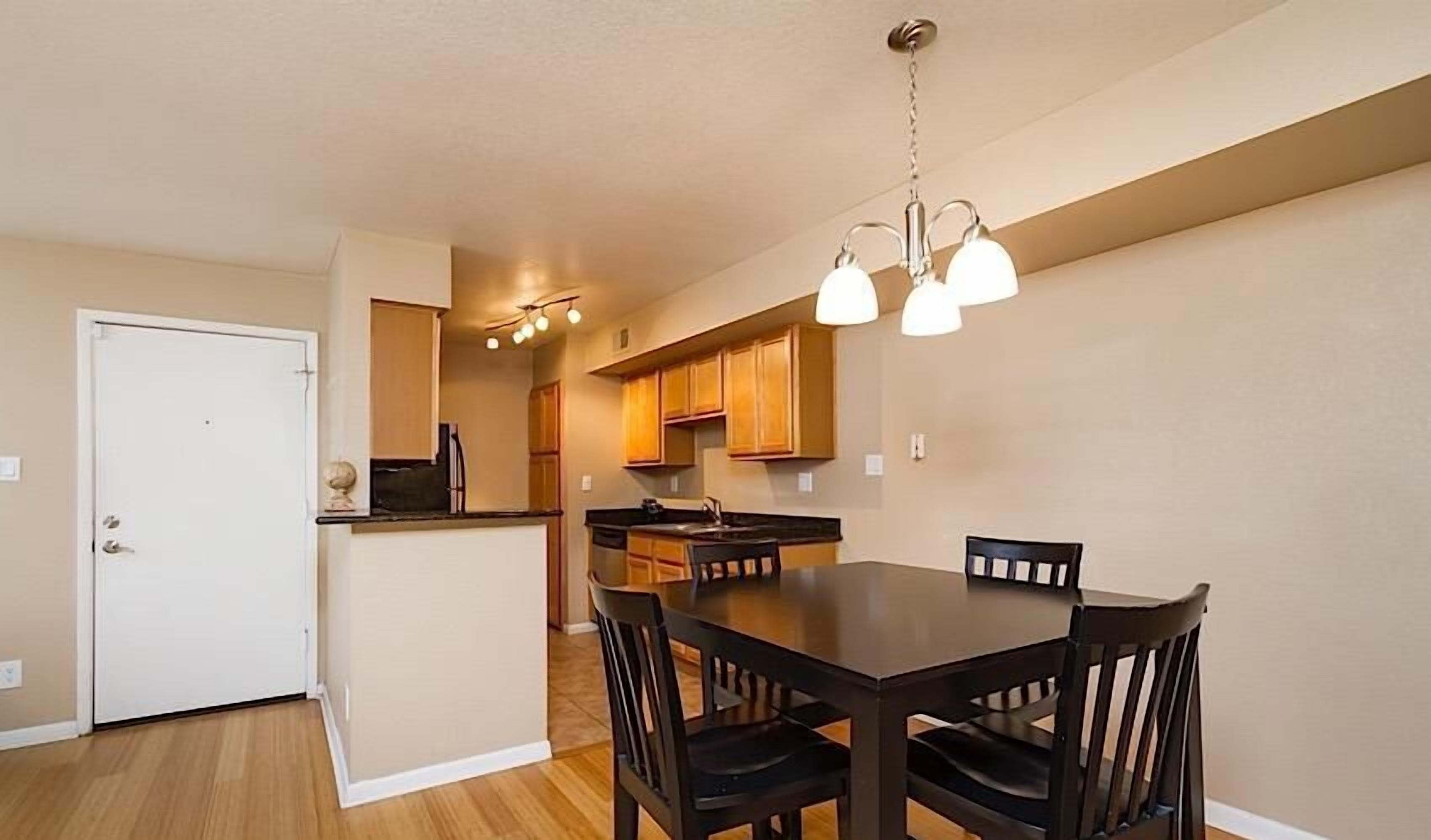 A compact kitchen with wooden cabinets, a dining table with chairs, and a hanging light fixture.