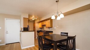A compact kitchen with wooden cabinets, a dining table with chairs, and a hanging light fixture. - Exclusively Yours By Signature Vacation Rentals (Scottsdale)