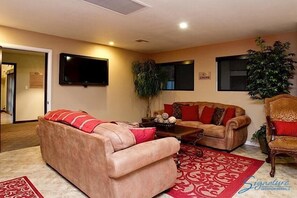 A living room with two sofas, a coffee table, and a television. There are plants and a sign on the wall. - Exclusively Yours By Signature Vacation Rentals (Scottsdale)