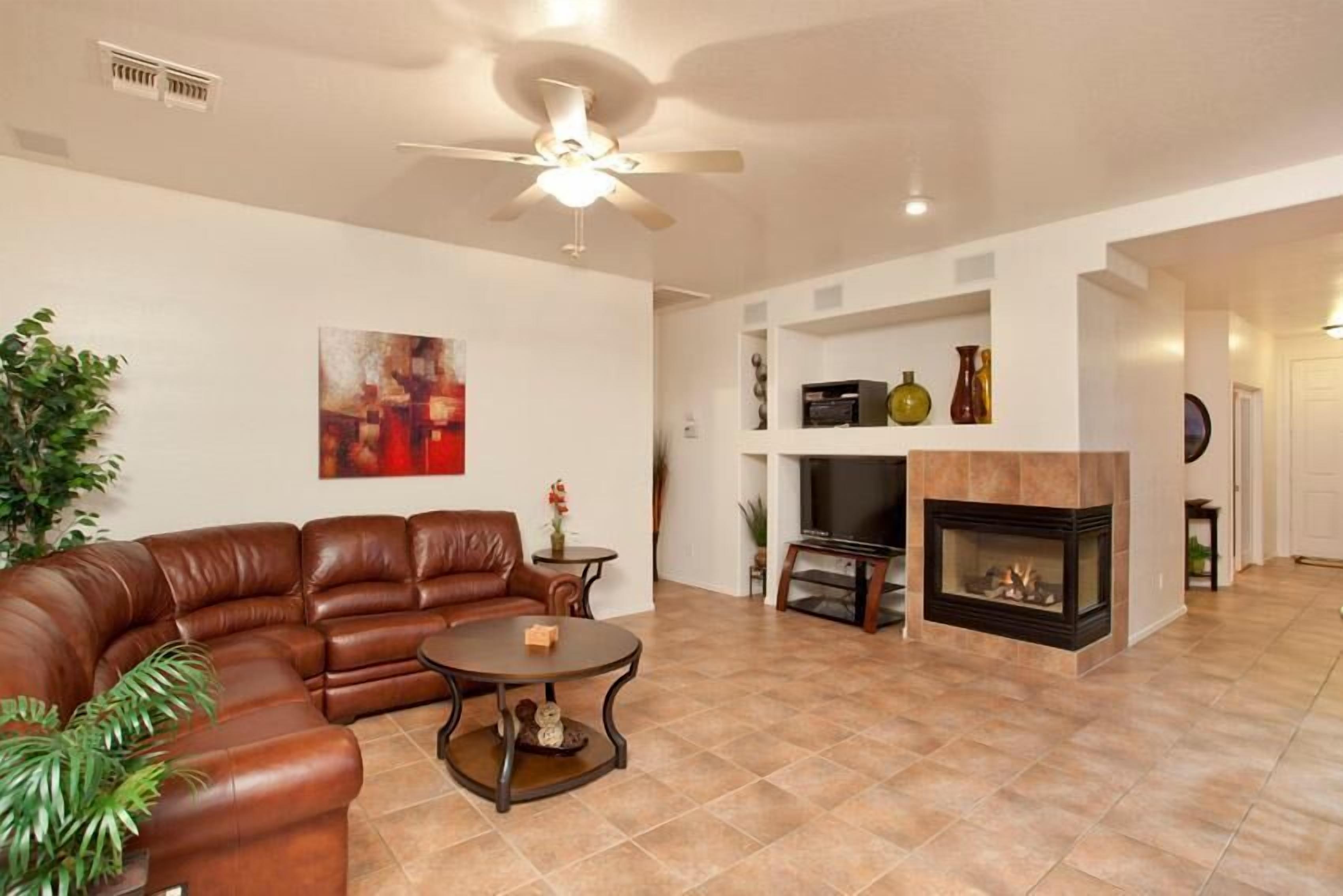 A living room with a brown leather sofa, a round coffee table, a fireplace, and a ceiling fan.