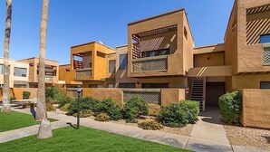 Um edifício residencial moderno de vários andares, com telhado plano, grandes janelas e um pátio com vegetação.