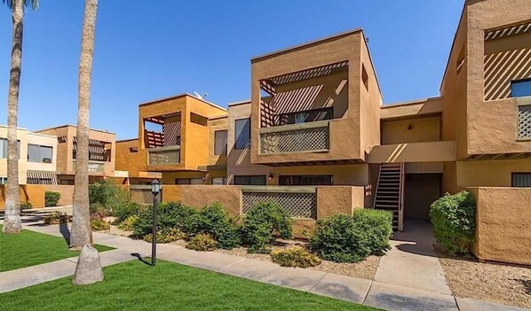 A modern multi-story residential building with a flat roof, large windows, and a courtyard with greenery.