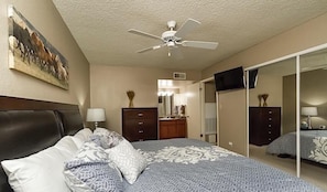 A bedroom with a bed, a ceiling fan, a dresser, a mirror, and a TV. - Endless Summer By Signature Vacation Rentals (Scottsdale)