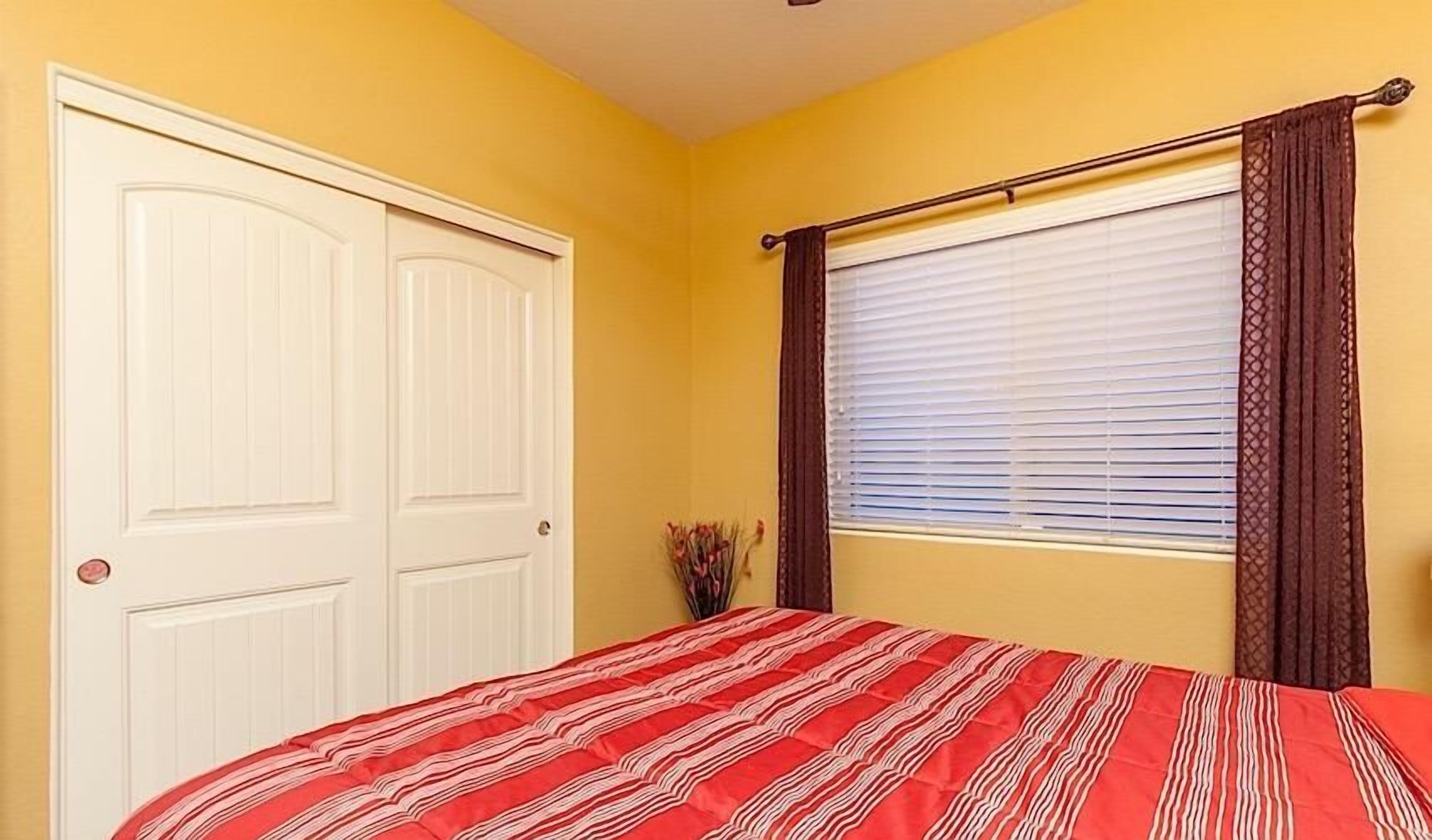 Ein Schlafzimmer mit einem Bett, einem Fenster mit Jalousien, einer Tür und einer Vase mit Blumen.