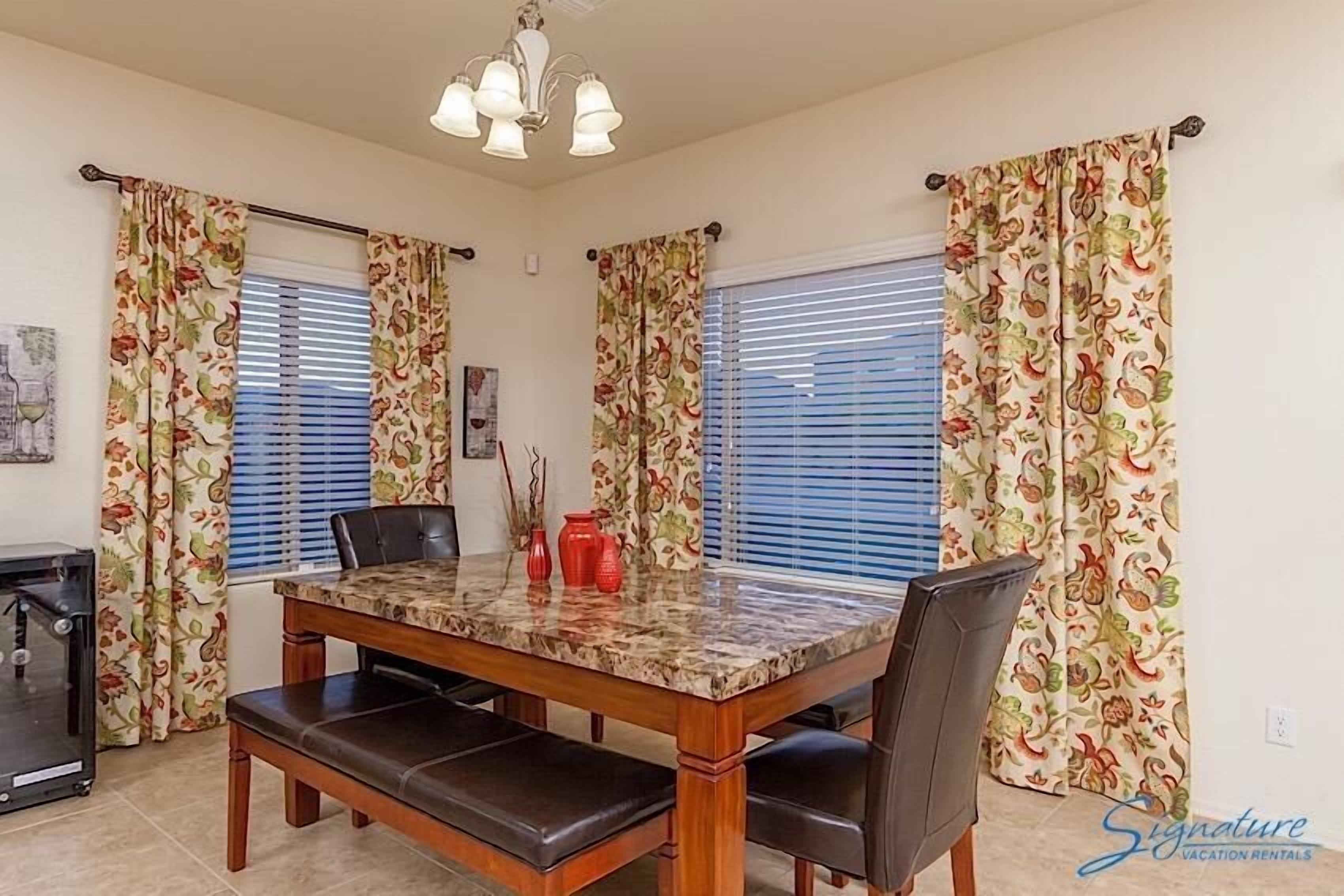 Een eetruimte met een houten tafel en stoelen, een kroonluchter en behang met een patroon.