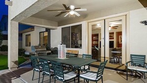 Un patio al aire libre con una mesa de comedor, sillas, un ventilador de techo y una parrilla.