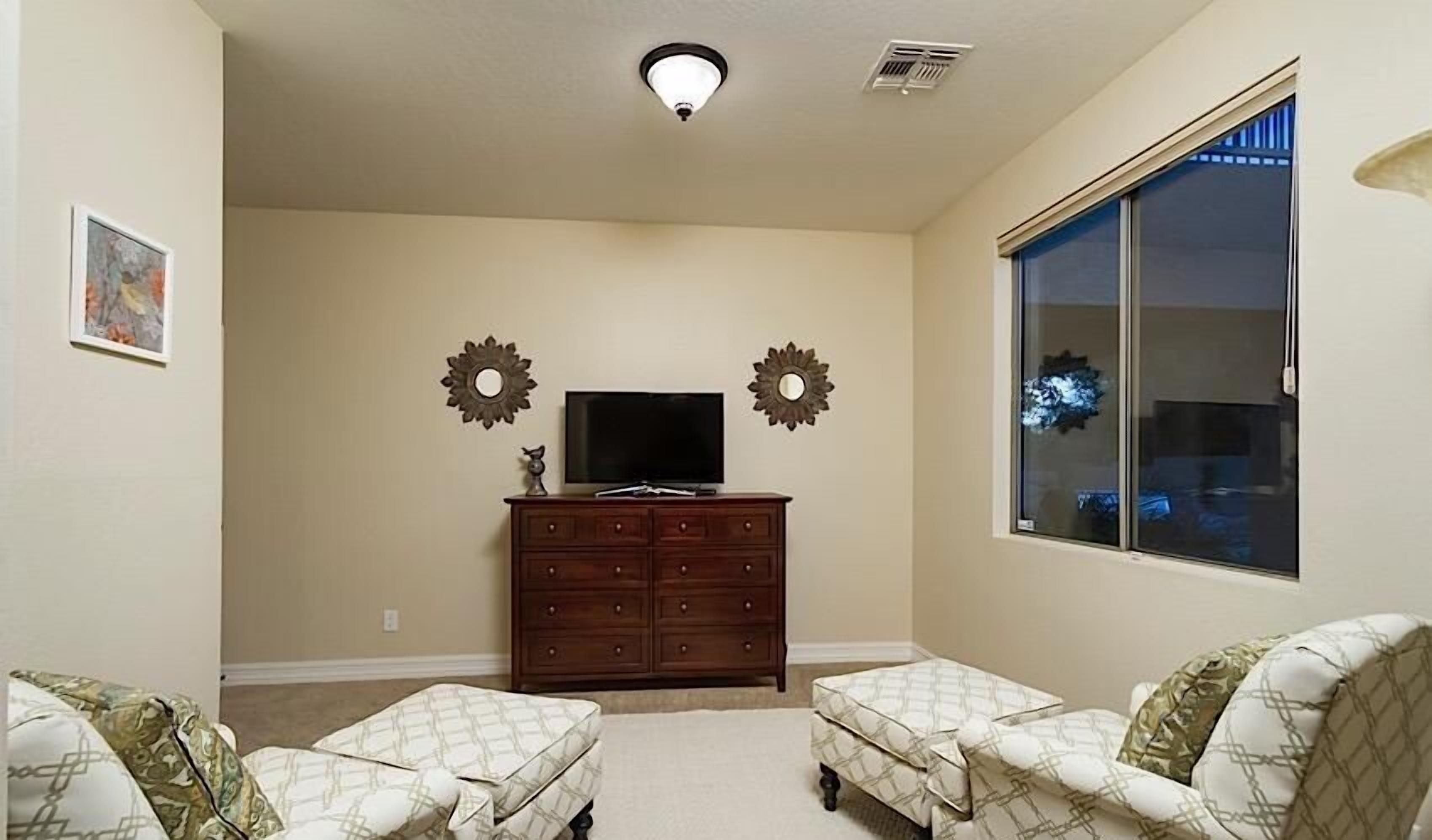 A living room with a television on a dresser, two armchairs, and decorative wall mirrors.
