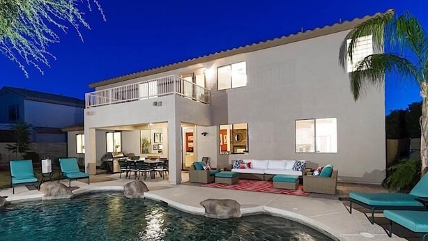 Una casa de dos pisos con piscina, mobiliario exterior y un balcón.