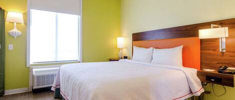 A hotel room with a large bed, two bedside lamps, a nightstand with a phone, and a window with blinds.