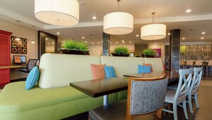 A modern restaurant with a green booth seating area, wooden tables, and chairs. - Home2 Suites by Hilton Portland (Portland)