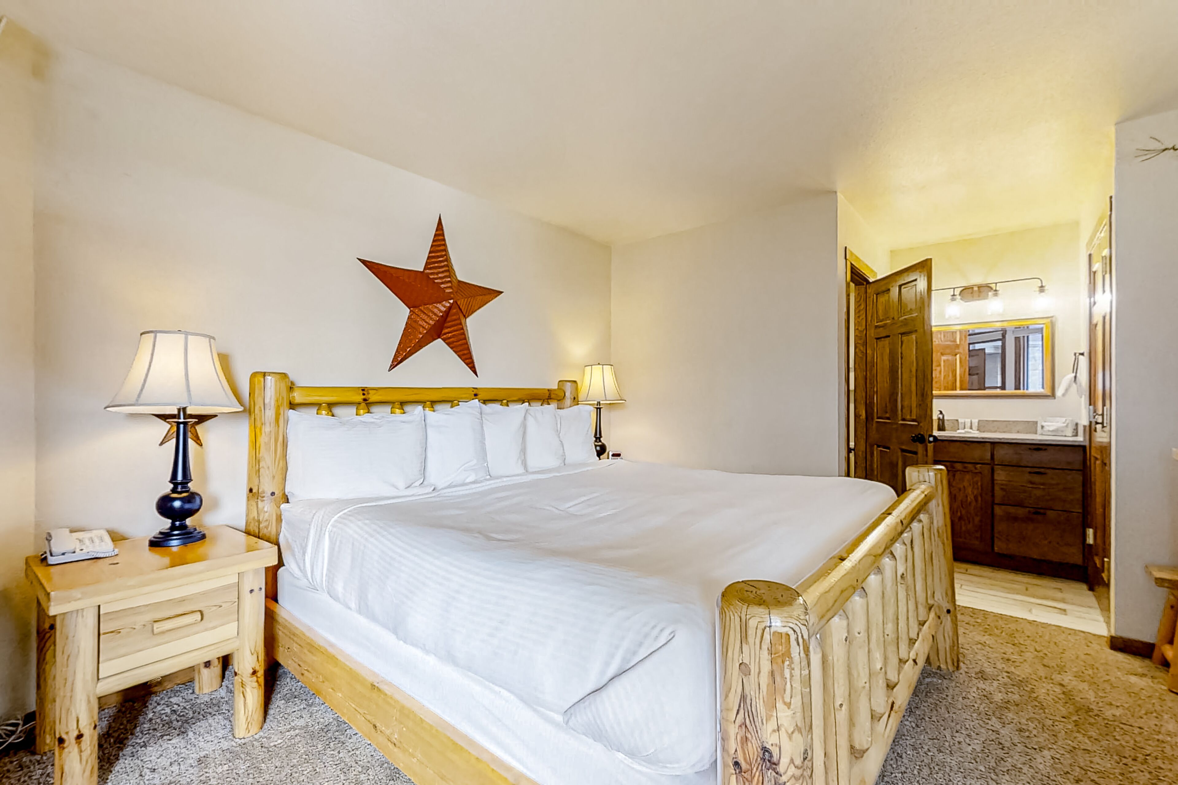 Une chambre d’hôtel avec un grand lit, une tête de lit en bois, deux tables de chevet avec des lampes, une décoration en forme d’étoile sur le mur et une salle de bain visible à travers une porte ouverte.
