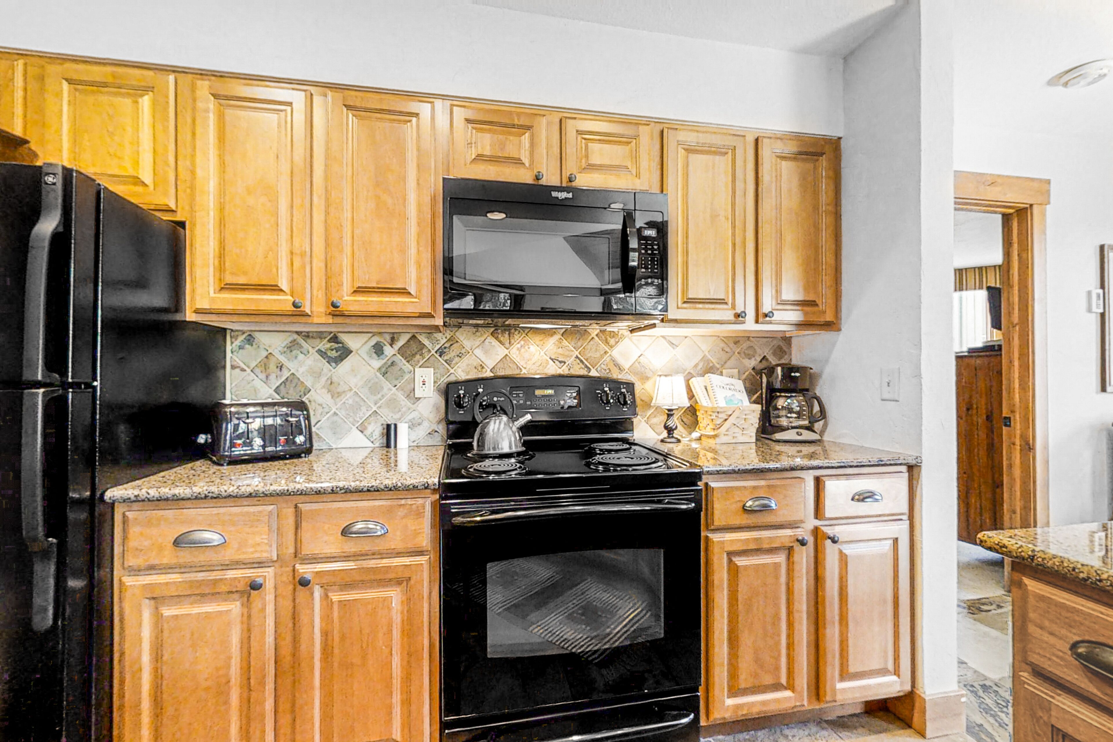 A kitchen with wooden cabinets, a black refrigerator, a microwave, a stove, and a toaster.