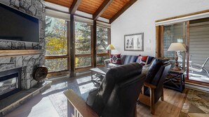 A spacious living room with a stone fireplace, leather furniture, large windows, and a wooden ceiling. - The Lodge at Steamboat (Steamboat Springs)