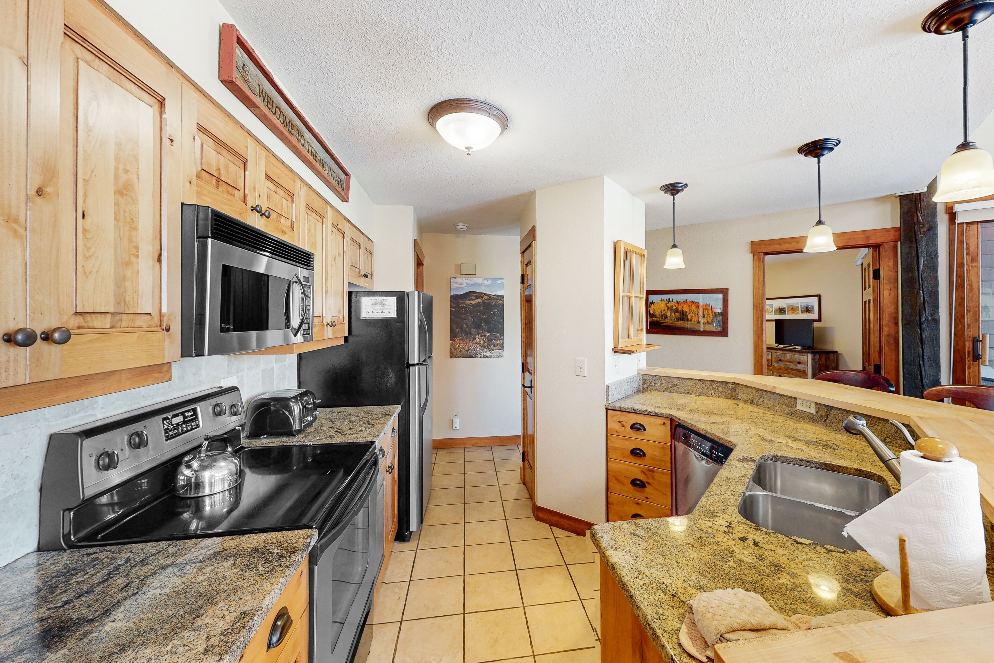 A kitchen with wooden cabinets, stainless steel appliances, granite countertops, and a view of the living area.