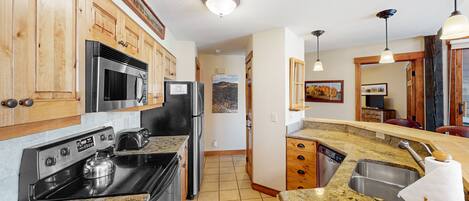 A kitchen with wooden cabinets, stainless steel appliances, granite countertops, and a view of the living area.
