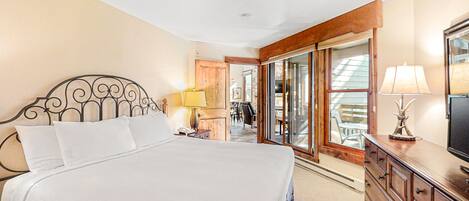 A bedroom with a large bed, wooden dresser, and a sliding glass door leading to a balcony.