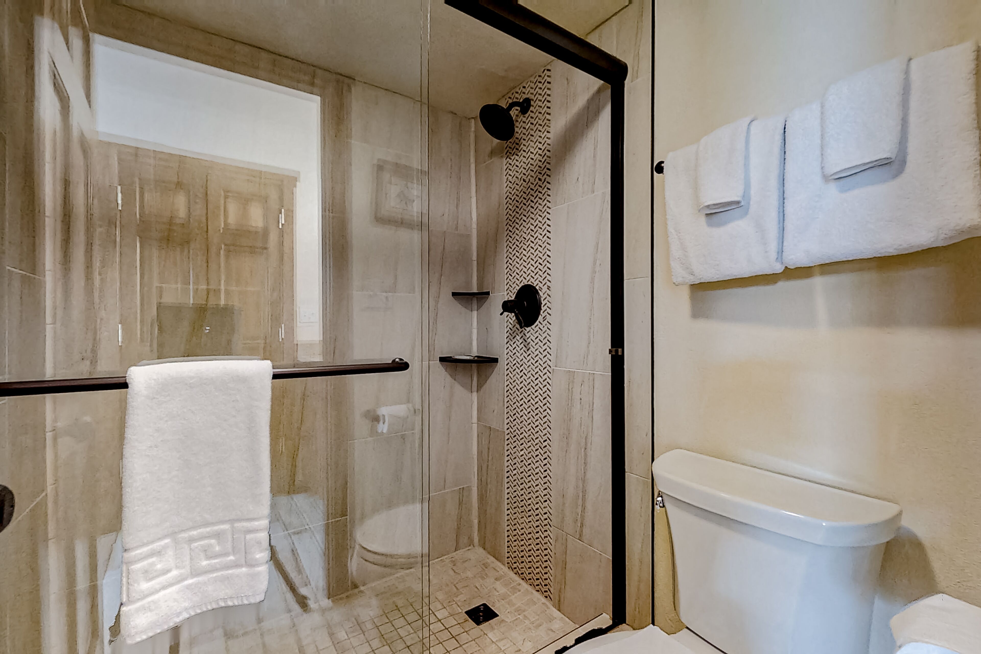 A modern bathroom with a glass-enclosed shower, a toilet, and a towel rack with multiple towels.