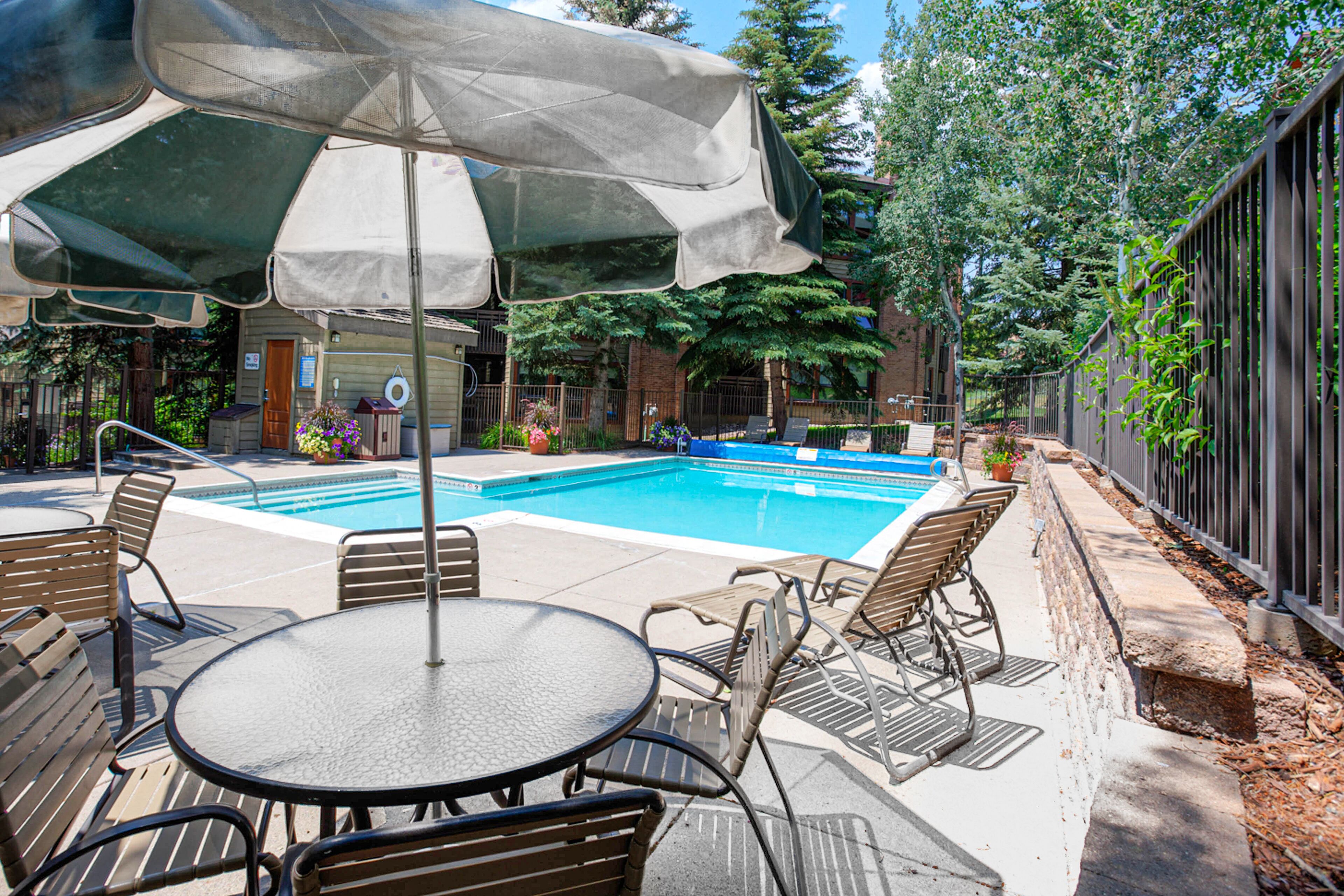 A backyard with a swimming pool, patio chairs, a table, and an umbrella.