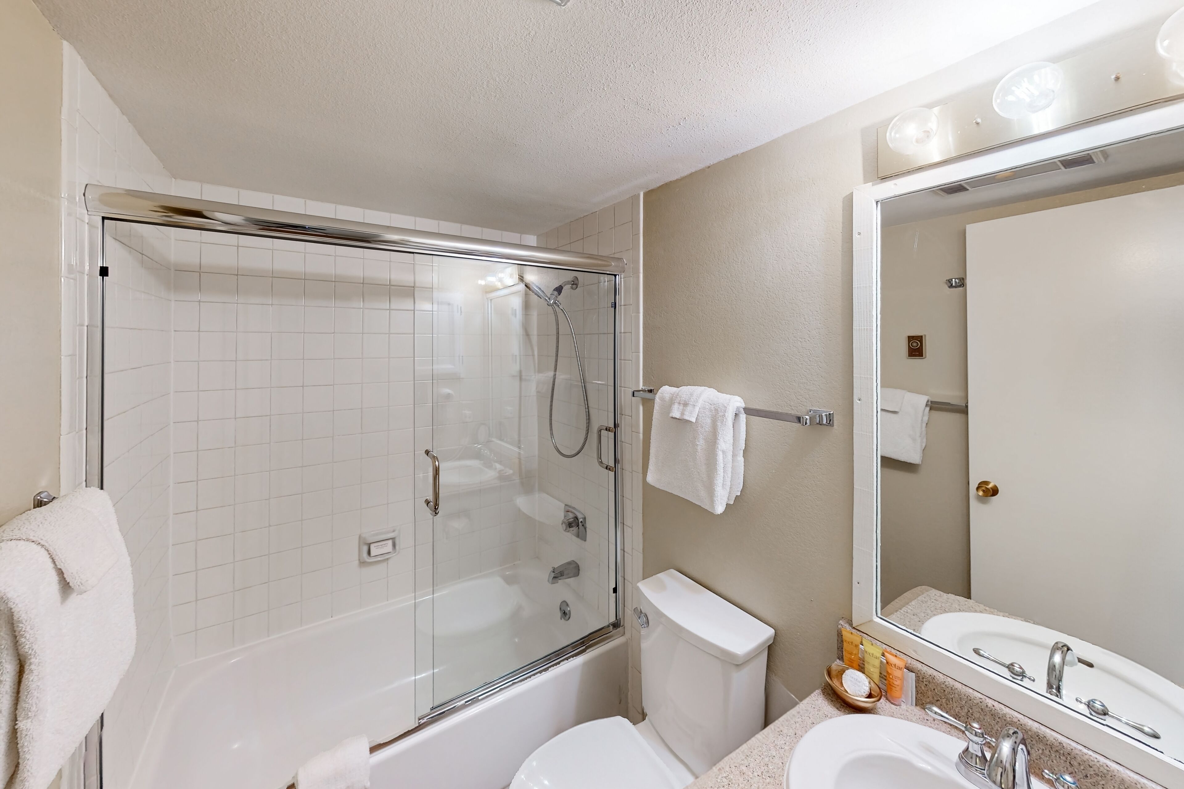 A bathroom with a glass-enclosed shower, a white toilet, a sink, and a mirror.