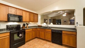 A kitchen with wooden cabinets, a black microwave, stove, and dishwasher. - Western Belle By Signature Vacation Rentals (Surprise)