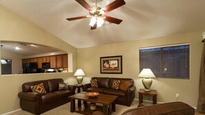 A living room with two brown leather sofas, a coffee table, a ceiling fan, and a window with blinds. - Western Belle By Signature Vacation Rentals (Surprise)