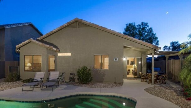 A house with a swimming pool, a covered patio, and a well-lit interior. - Western Belle By Signature Vacation Rentals (Surprise)