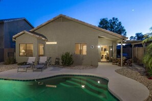 A house with a swimming pool, a covered patio, and a well-lit interior. - Western Belle By Signature Vacation Rentals (Surprise)