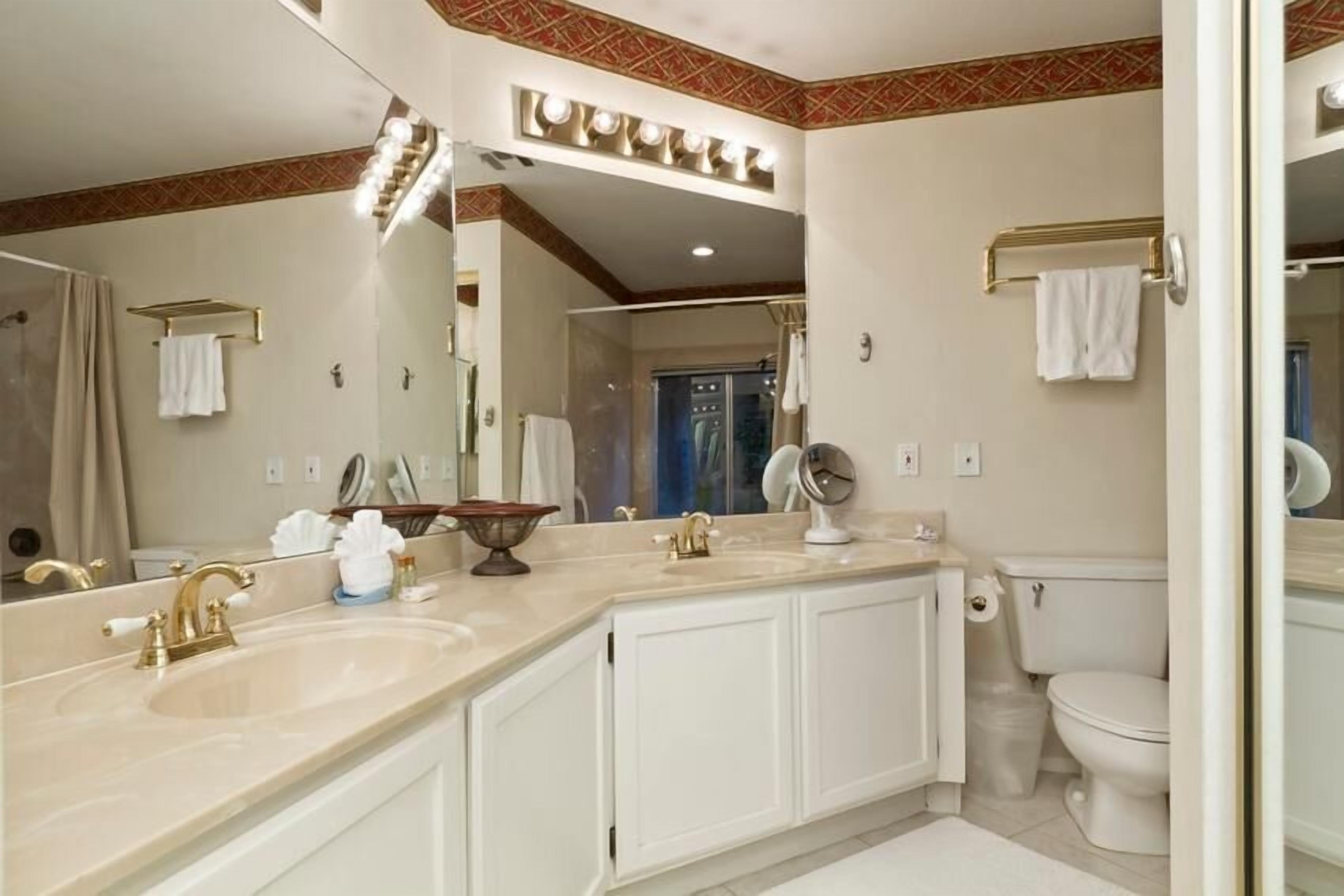 A bathroom with a large mirror, two sinks, a toilet, and a shower area.