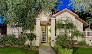 A two-story house with a front entrance, a garage, and a well-maintained garden with various plants and a pathway leading to the door.