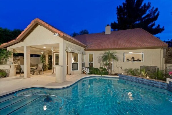 A residential property with a swimming pool, covered patio, and a house with a tiled roof.