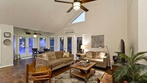 A spacious living room with a ceiling fan, a large window, and a dining area with a table and chairs. - Velvet Dream By Signature Vacation Rentals (Tempe)