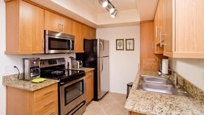 A compact kitchen with wooden cabinets, stainless steel appliances, granite countertops, and a double sink. - Ultra Chic and Modern By Signature Vacation Rentals (Scottsdale)