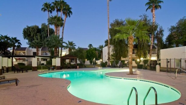 A swimming pool with a curved edge, surrounded by palm trees and lounge chairs. - Ultra Chic and Modern By Signature Vacation Rentals (Scottsdale)