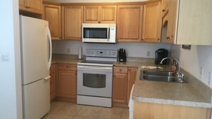 Una cocina con armarios de madera, un refrigerador blanco, un microondas, un horno y un lavamanos.
