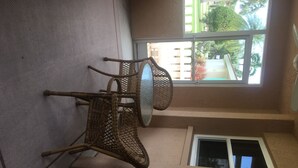 Una habitación con techo alto, ventana con vista a palmeras y un pequeño balcón con puerta blanca.