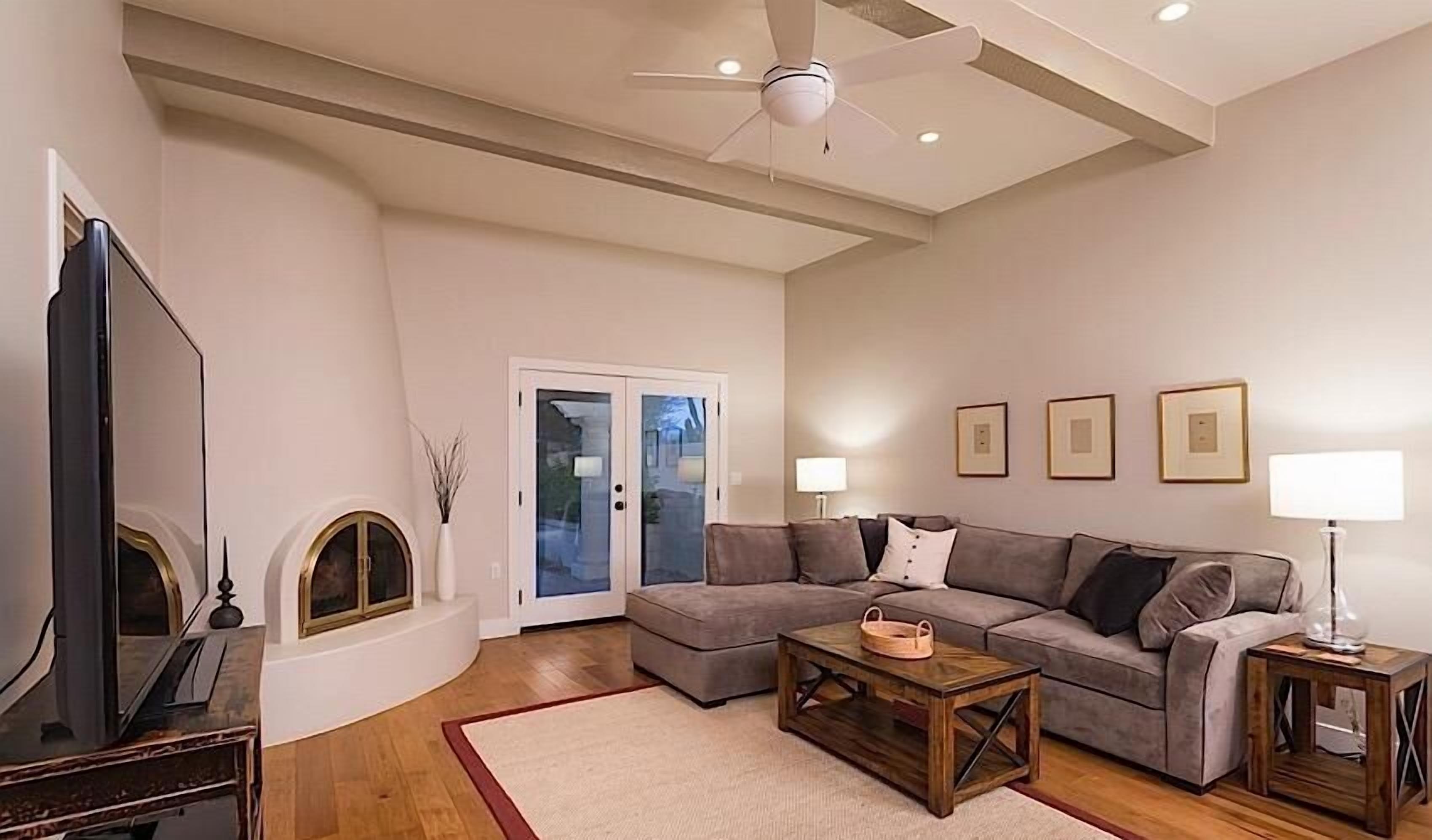 Un salon avec un canapé gris, une table basse en bois, un téléviseur et un ventilateur de plafond.